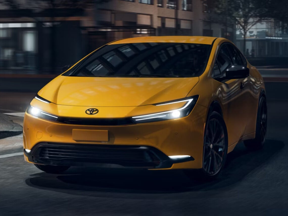 Front three-quarter shot of a yellow Toyota Prius Nightshade driving on a city street at night.