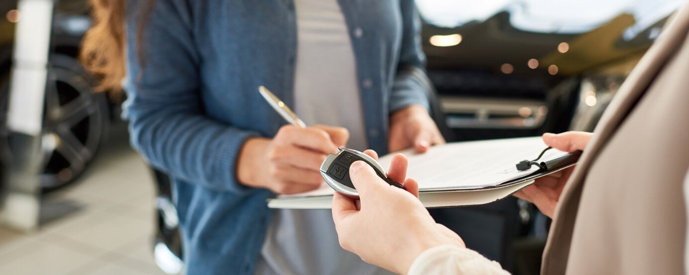 Customer signs vehicle purchase paperwork while a dealership representative hands over a key fob.