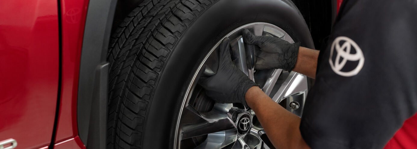 Toyota technician install an alloy wheel on a red vehicle during dealership service.