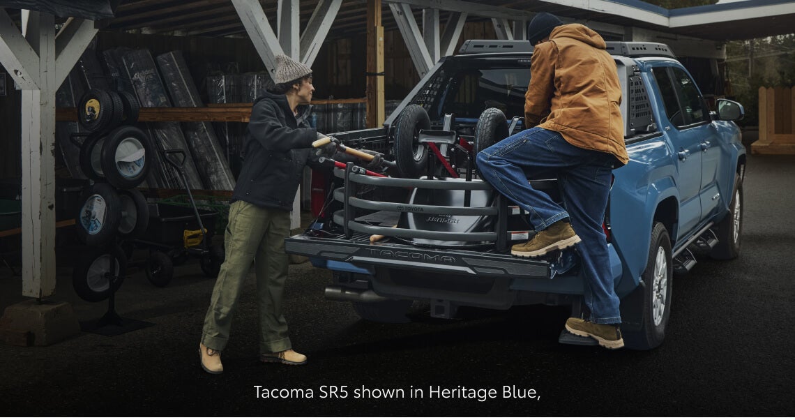 Rear view of a Toyota Tacoma SR5 in Heritage Blue with people loading outdoor gear into the truck bed.