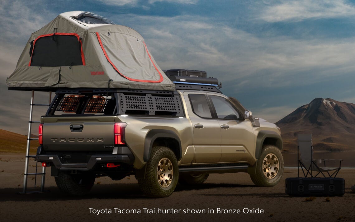Rear three-quarter view of a Toyota Tacoma Trailhunter in Bronze Oxide with an open rooftop tent setup.