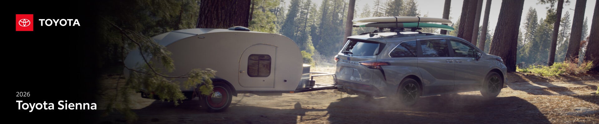 A gray Toyota Sienna Tows a trailer down a lakeside forest road.