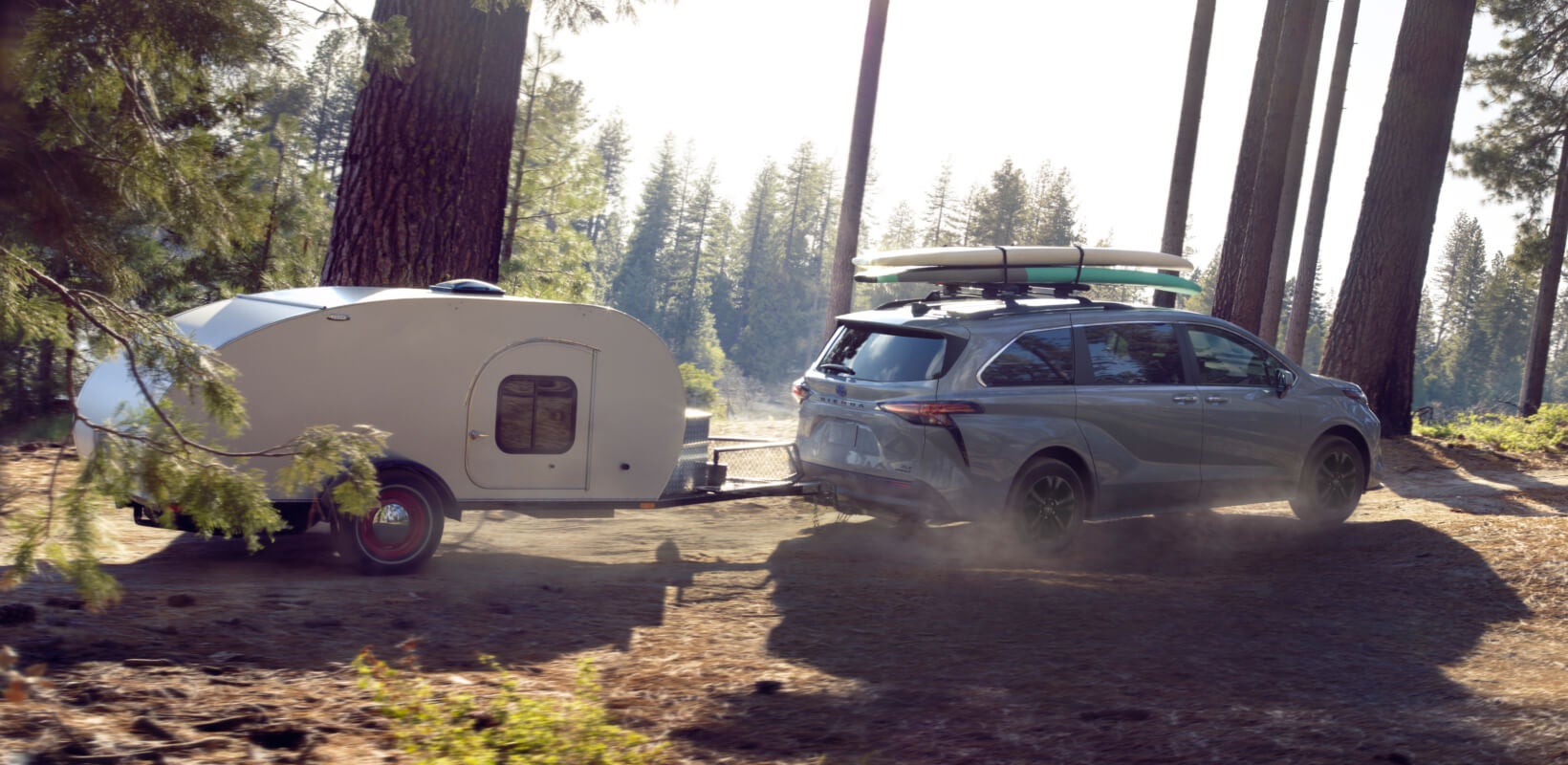 A gray Toyota Sienna Tows a trailer down a lakeside forest road.
