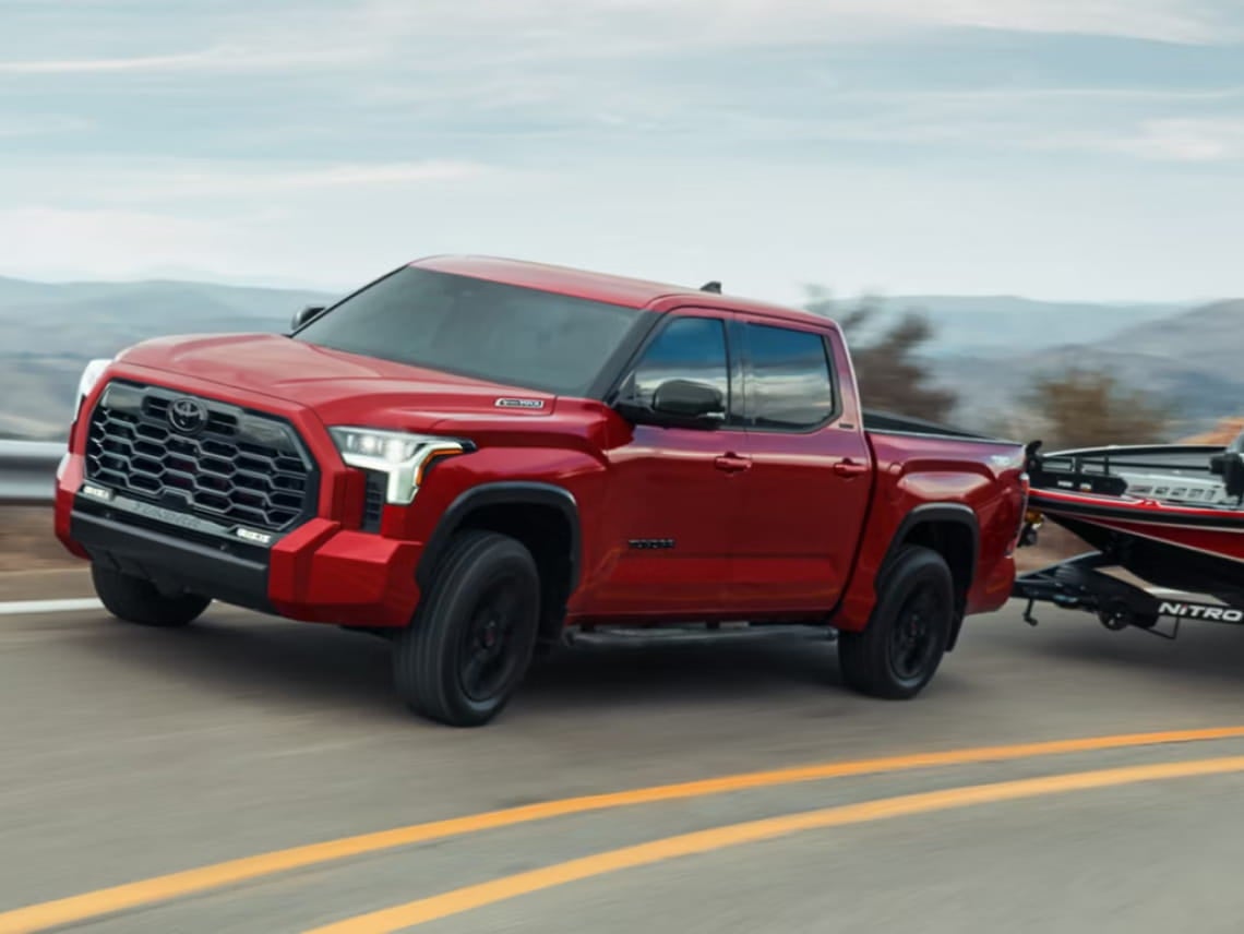 Red Toyota Tundra towing a boat on a highway.