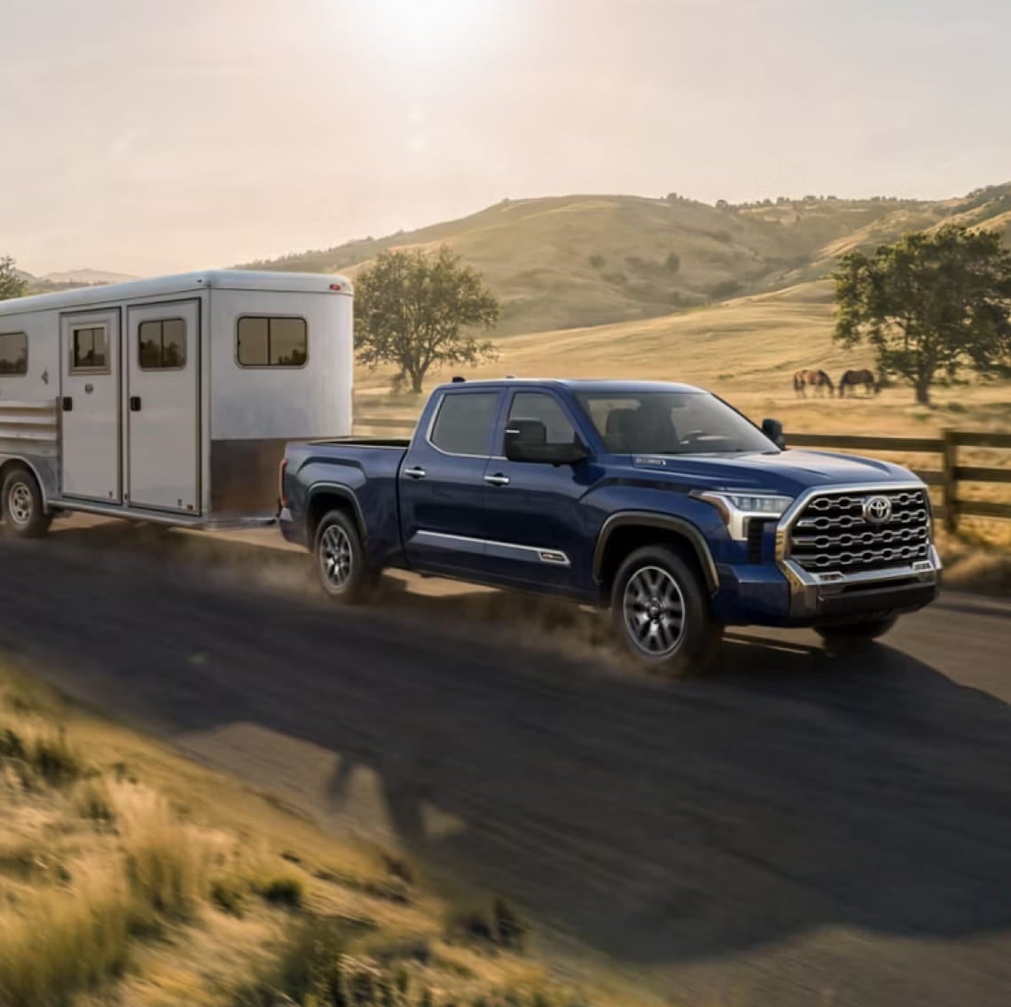 Blue Toyota Tundra towing a horse trailer on a country road.
